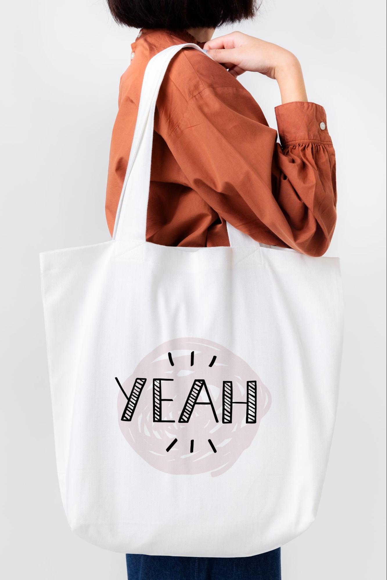 Person carrying custom tote bag with 'YEAH' design